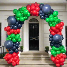 Load image into Gallery viewer, A colorful organic balloon arch blocked in red, green, and blue, standing in front of a doorway.
