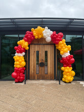 Load image into Gallery viewer, A balloon garland arch in red, yellow, and white balloons decorated around a wooden double door on a building entrance.