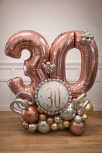 Load image into Gallery viewer, Rose gold and silver '30' balloon decoration on a wooden surface with a white wall background.

