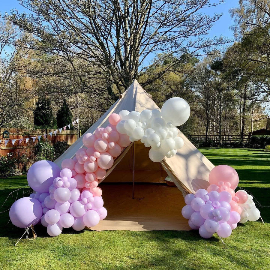 Teepee tent decorated with pink, purple, and white balloons in a garden setting.