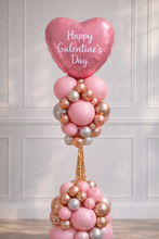 Load image into Gallery viewer, Balloon arrangement with a pink heart-shaped balloon reading 'Happy Valentine's Day' against a white paneled wall.
