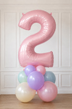 Load image into Gallery viewer, Pink number 2 balloon with smaller pastel balloons on a wooden floor against a white paneled wall.
