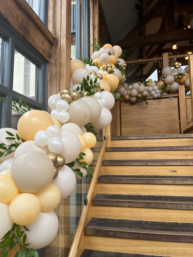 Decorative balloon arch with white, gold, and green balloons in a rustic wooden interior.