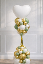Load image into Gallery viewer, Balloon arrangement with a heart-shaped balloon and gold, green, and white balloons against a white paneled wall.
