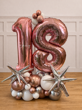 Load image into Gallery viewer, Rose gold number '18' balloons with decorative stars and smaller balloons and starburst balloons on a wooden floor.
