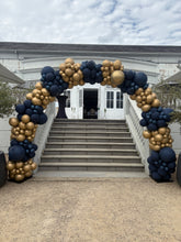 Load image into Gallery viewer, A balloon garland arch decorated with navy blue and metallic gold balloons, set up outdoors in front of a building with wide stone steps.
