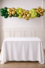 Load image into Gallery viewer, Balloon arch with green and gold balloons above a white table.
