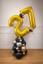 Load image into Gallery viewer, Gold number 21 balloon with smaller balloons below against a white paneled wall.
