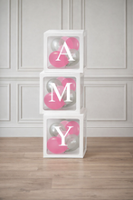 Load image into Gallery viewer, Stack of white boxes with pink and gray balloons spelling out 'AMY' against a light gray paneled wall.
