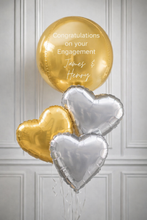 Load image into Gallery viewer, Gold and silver heart-shaped balloons with 'Congratulations on your Engagement' text against a gray paneled wall.
