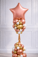 Load image into Gallery viewer, Decorative balloon arrangement with a rose gold star at the top against a white paneled wall.
