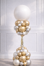 Load image into Gallery viewer, Decorative balloon sculpture with gold, silver, and white balloons against a white paneled wall.
